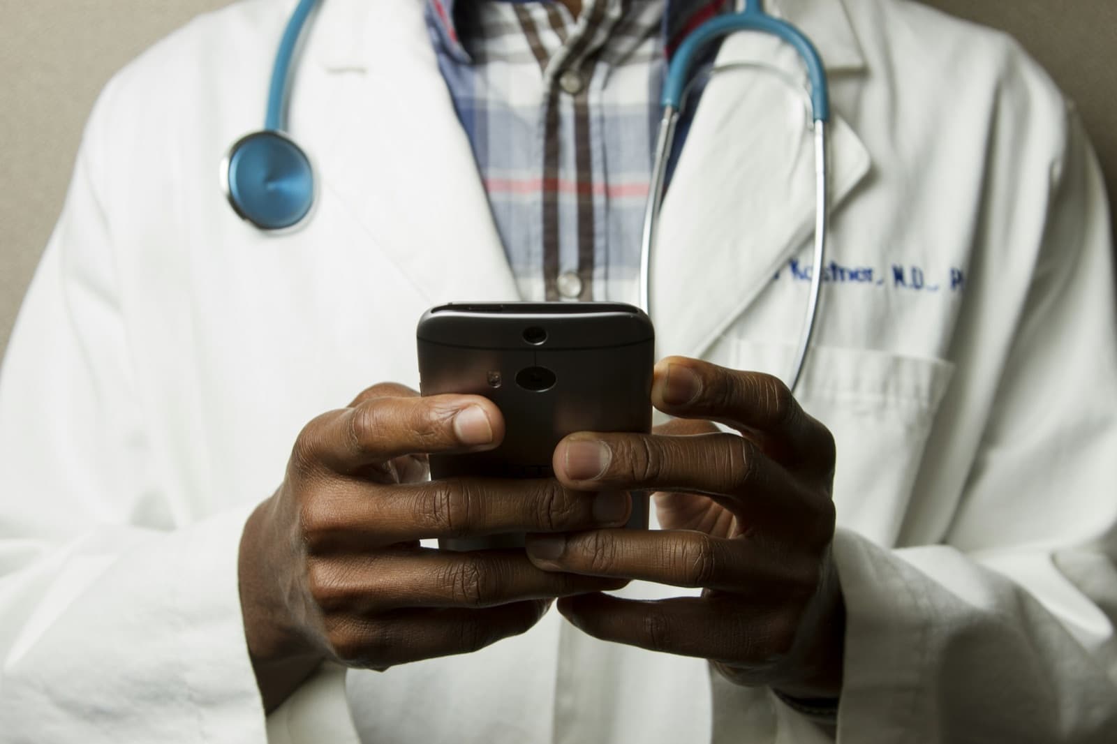 A healthcare professional in a white coat with a stethoscope, reviewing content on a phone